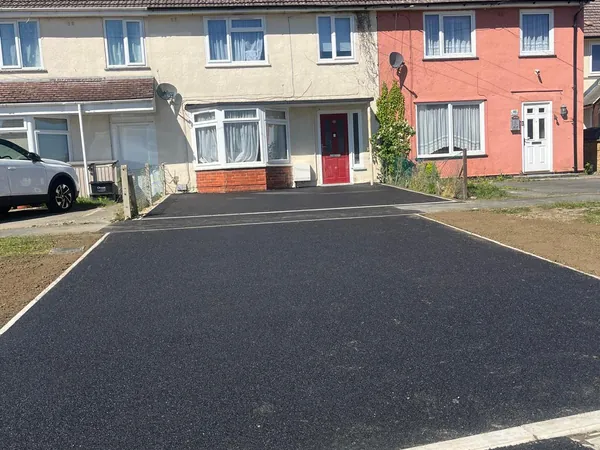 New black tarmac driveway with a light edging line in front of terraced houses